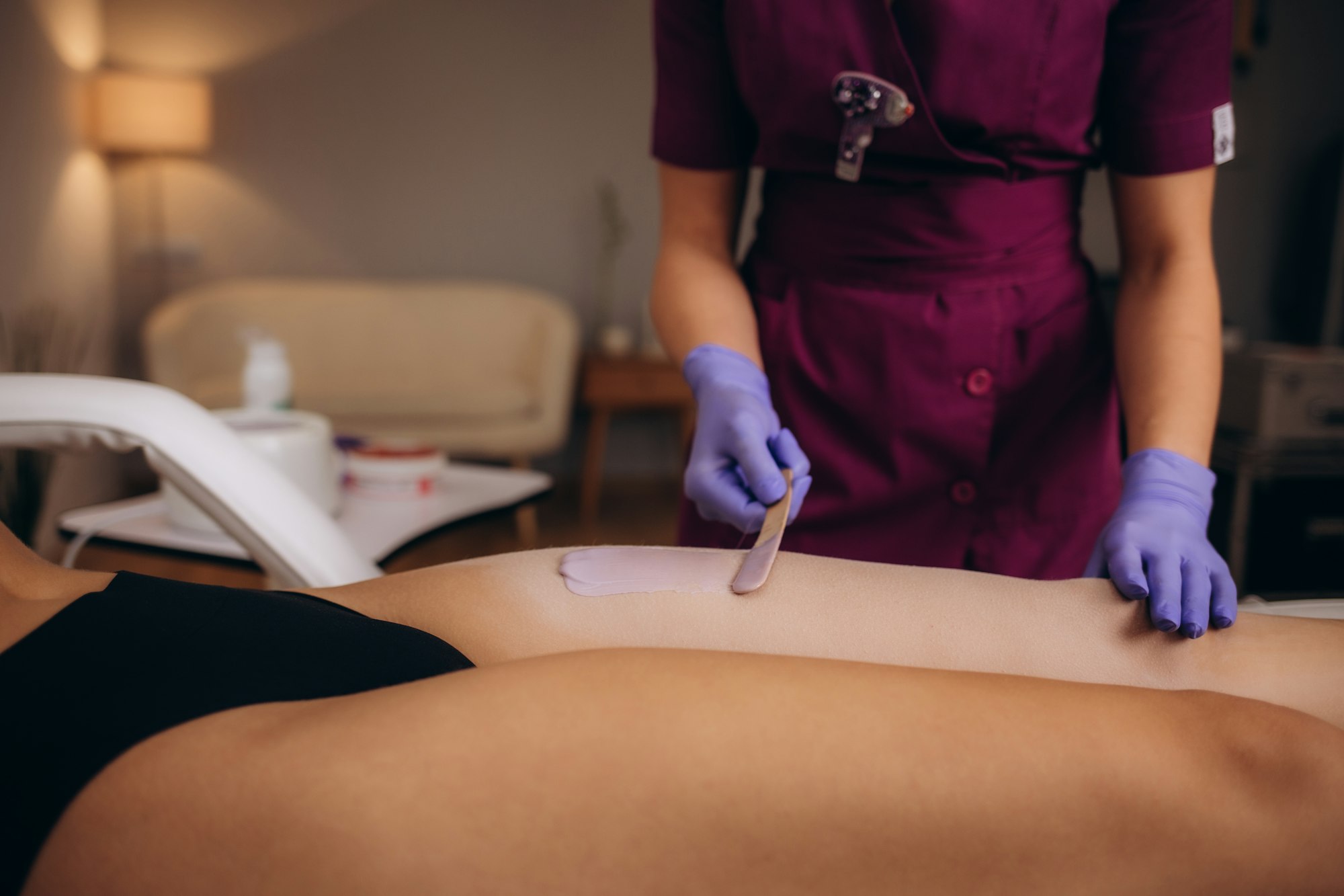 A master applies pink depilatory wax to a young woman's leg for hair removal. Depilation with wax.