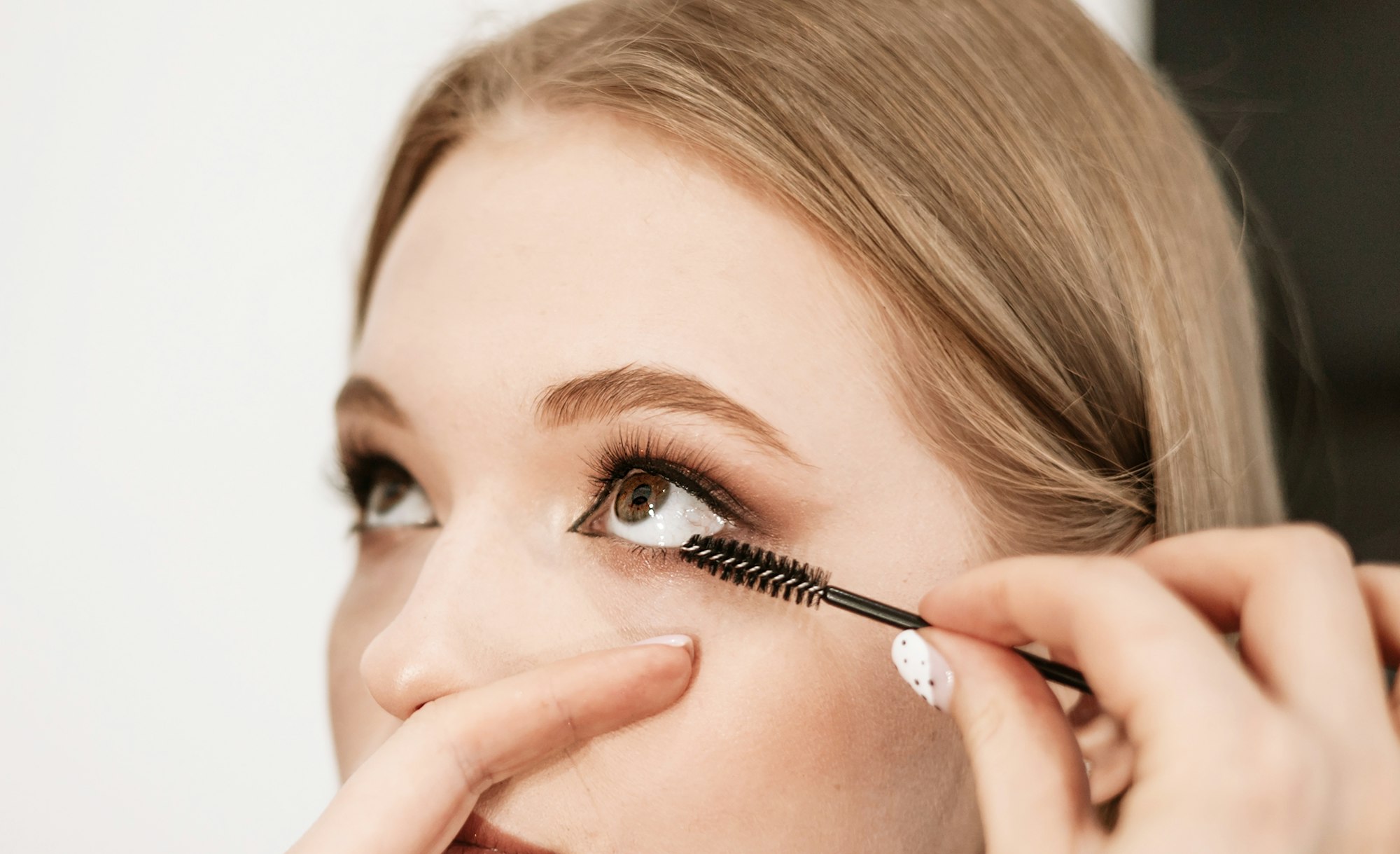 makeup artist applies mascara to lashes on a beautiful young woman blonde model, face make up